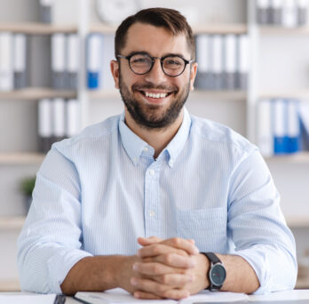 Graduate from an online degree program is smiling while wearing glasses and a blue button up while being interviewed. 