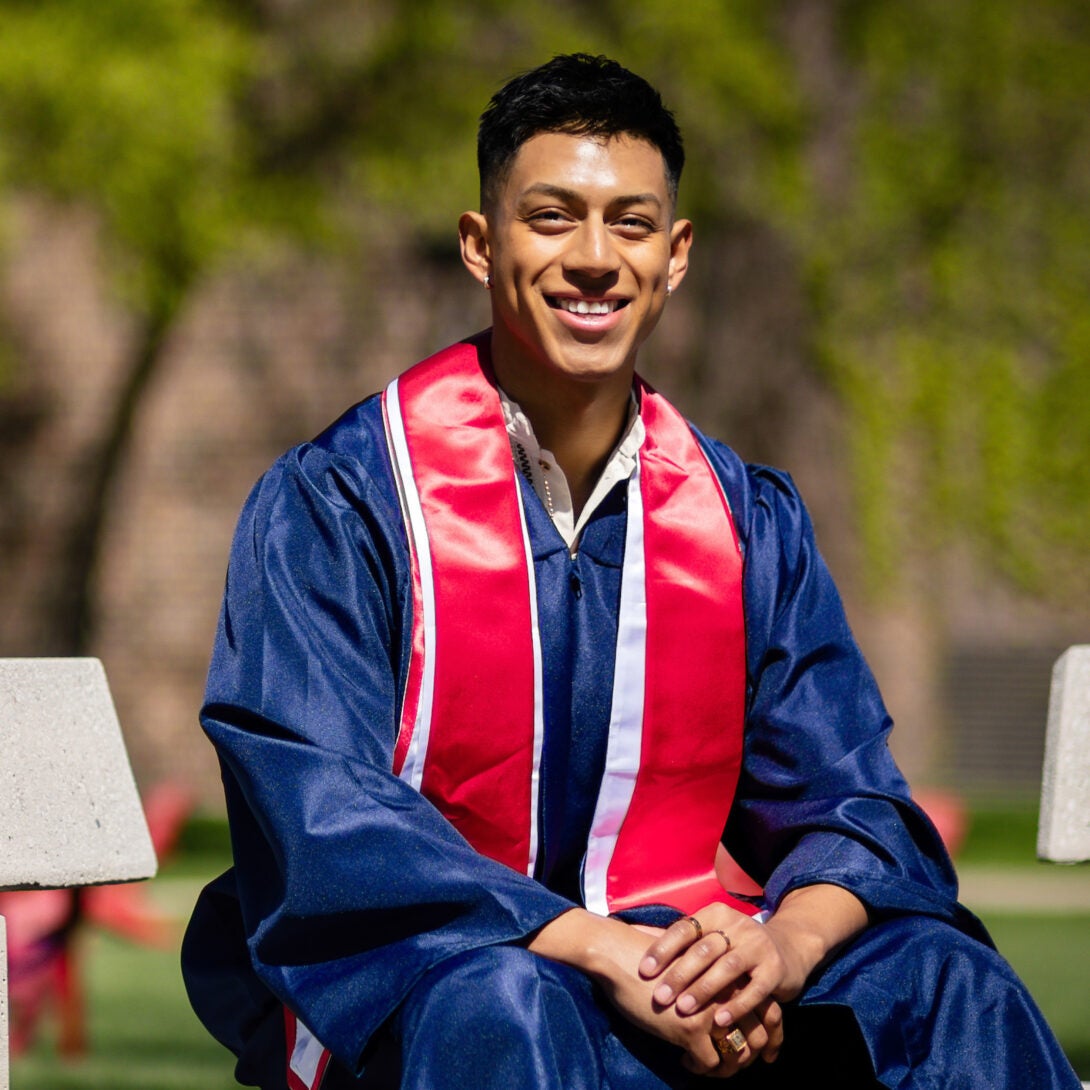 UIC graduate smiles outside on bench