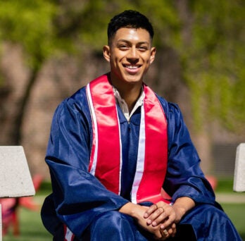 UIC graduate smiles outside on bench 